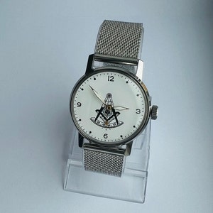 May include: A silver watch with a white face and a silver mesh band. The face of the watch features a black and white compass and the numbers 12, 3, 6, and 9.