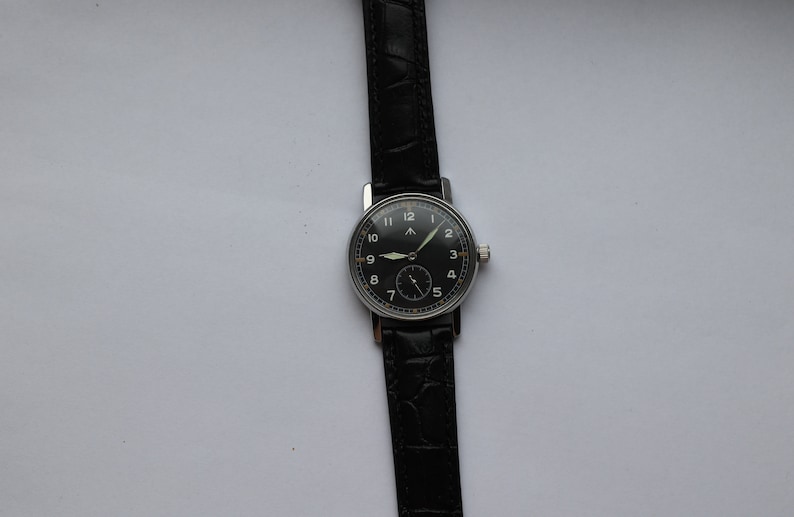 May include: A black-faced wristwatch with silver hands and numerals on a black leather band.