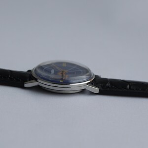 Puede incluir: Un reloj de pulsera plateado con una esfera azul y una correa de cuero negra.