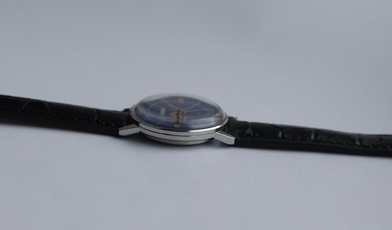 Puede incluir: Un reloj de pulsera plateado con una esfera azul y una correa de cuero negra.