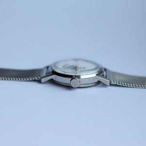 May include: A silver wristwatch with a white face and a silver mesh band.