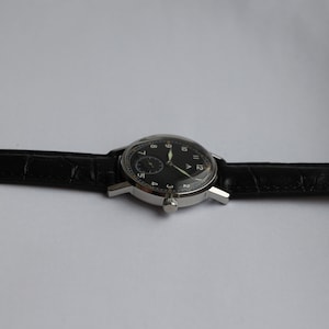 May include: A silver wristwatch with a black face and white numerals. The watch has a black leather band.