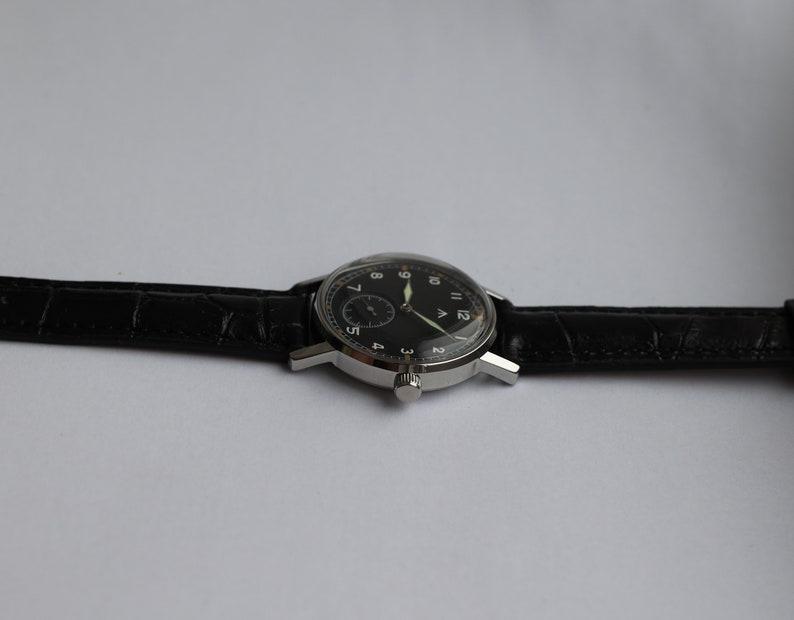 May include: A silver wristwatch with a black face and white numerals. The watch has a black leather band.