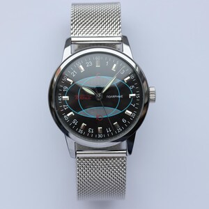 May include: A silver-toned wristwatch with a black face featuring a unique design with blue and red accents. The watch has a mesh band and a dial with numbers and text, including the word "Polarnye".