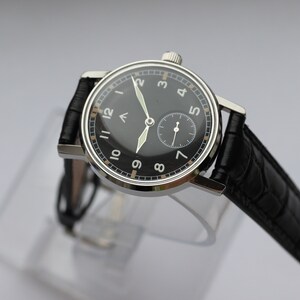 May include: A black-faced wristwatch with white numerals and a black leather band. The watch has a small seconds dial at the 6 o'clock position.