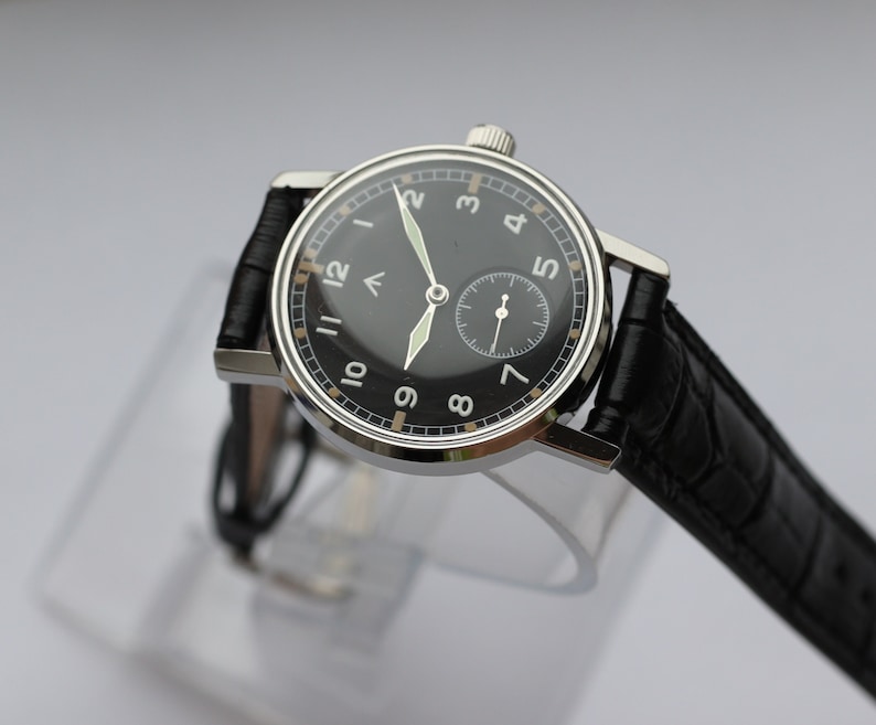 May include: A black-faced wristwatch with white numerals and a black leather band. The watch has a small seconds dial at the 6 o'clock position.