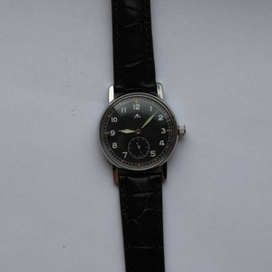 May include: A black-faced wristwatch with white numerals and a black leather band. The watch has a silver case and a small second hand.