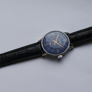 Puede incluir: Un reloj de pulsera plateado con una esfera azul y marcas doradas. El reloj tiene una correa de cuero negro con un patr&oacute;n de cocodrilo.