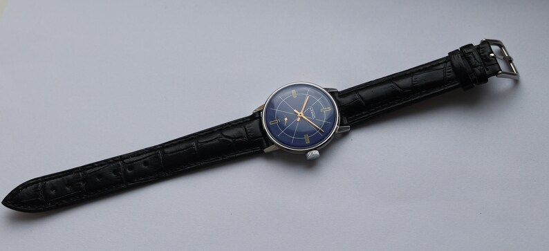 Puede incluir: Un reloj de pulsera plateado con una esfera azul y marcas doradas. El reloj tiene una correa de cuero negro con un patr&oacute;n de cocodrilo.