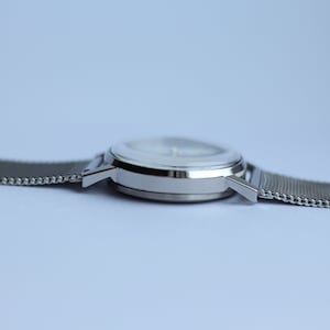 May include: A silver wristwatch with a white face and a silver mesh band.