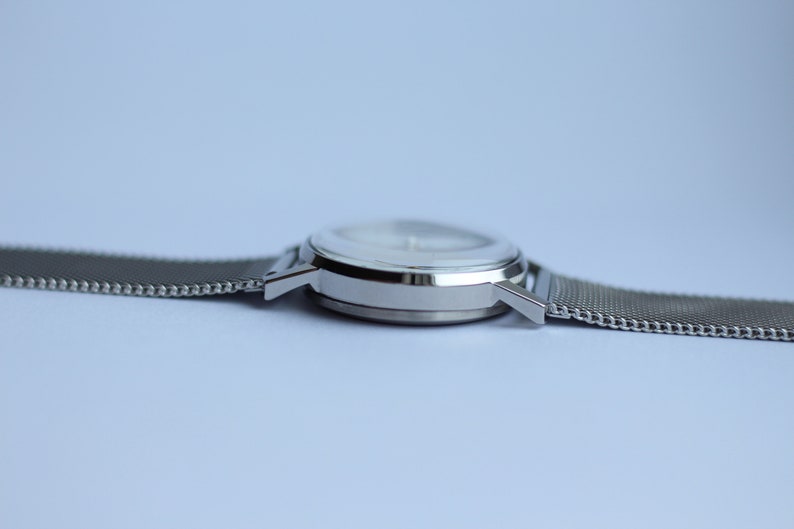 May include: A silver wristwatch with a white face and a silver mesh band.