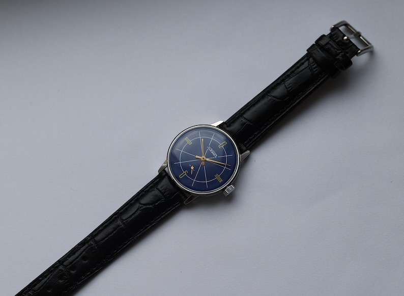 Puede incluir: Un reloj de pulsera vintage con una esfera azul y detalles dorados. El reloj tiene una correa de cuero negro con un patr&oacute;n de cocodrilo.