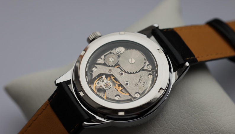 May include: A silver wristwatch with a black leather band and a clear case back revealing the inner workings of the watch. The watch face has the text "ЧЧ 2609" printed on it.