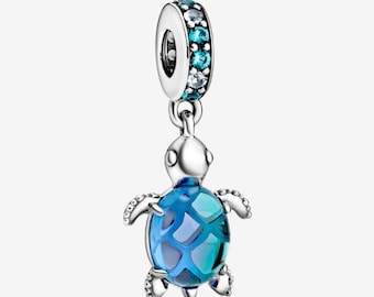 May include: A silver charm with a sea turtle design. The turtle has a blue and teal shell with a scale pattern. The charm's top has a ring with blue and clear gemstones, and it hangs from a silver loop.