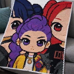 May include: A crocheted blanket featuring three anime-style characters with large eyes and colorful hair. The blanket has a white border and is draped over a gray sofa. The characters have purple, red, and blue hair.