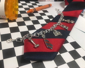 May include: A silver charm bracelet with a variety of charms, including a tie, a gavel, a camera, and a pair of glasses. The bracelet is lying on a red and blue striped tie.