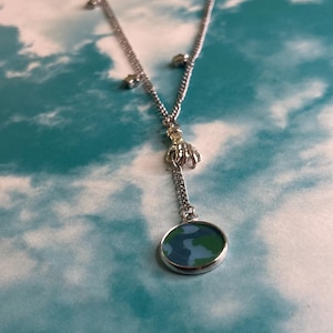 May include: Silver-toned necklace with a pendant featuring a circular design of blue and green. The necklace has small decorative accents along the chain. The pendant is approximately 0.75 inches in diameter.