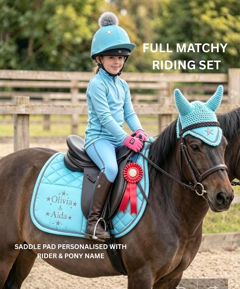 May include: A light blue equestrian riding set featuring a quilted saddle pad personalized with the text Olivia & Aida, a matching crochet ear bonnet with a star emblem, and a light blue riding helmet with a grey pom-pom and star details.