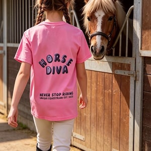 May include: A bright pink short-sleeved t-shirt featuring the dark purple text HORSE DIVA on the back, with the additional text NEVER STOP RIDING UNIQUE EQUESTRIAN EST. 2020 printed below in a smaller, dark purple font.