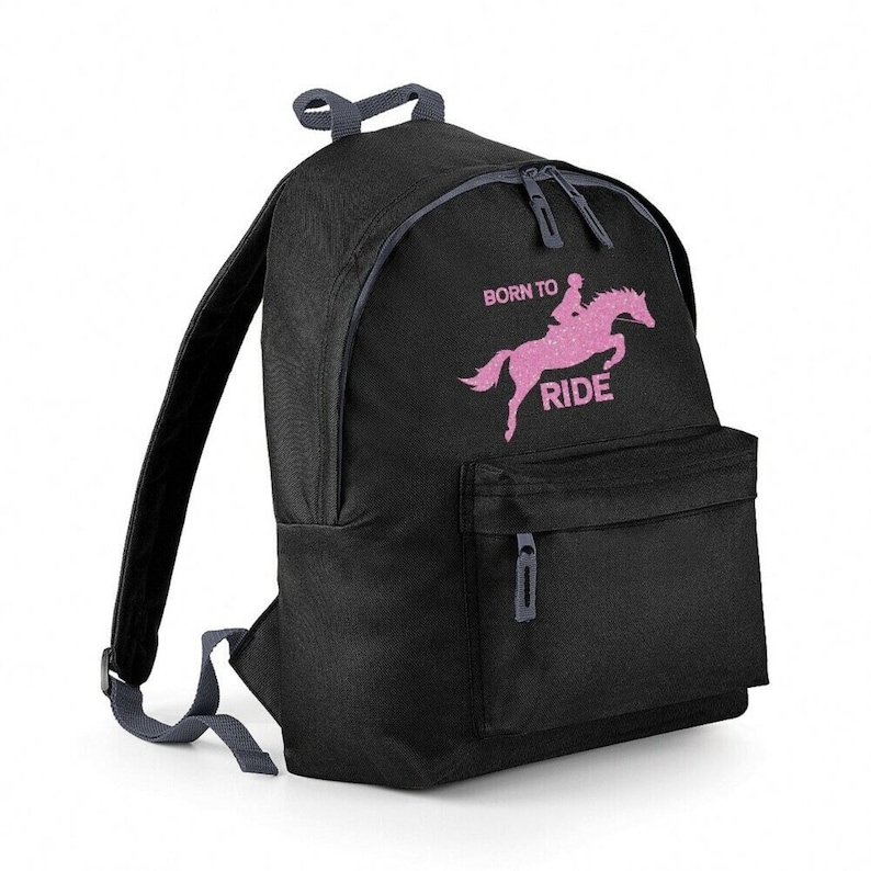 May include: Black backpack with a front pocket and two zippered compartments. The backpack features a pink glitter graphic of a horse and rider jumping, with the words "BORN TO RIDE" in pink.