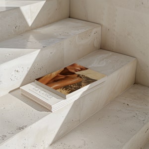 May include: A stack of magazines with a woman on the cover. The cover is white with the text "La Costa" in black. The magazines are sitting on a set of concrete stairs.
