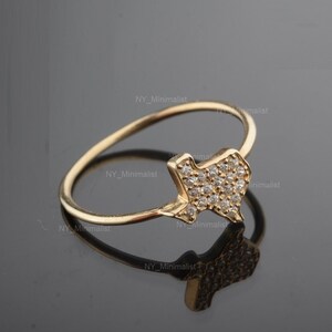 May include: A gold ring with a pave-set diamond Texas state outline. The ring is on a black reflective surface.
