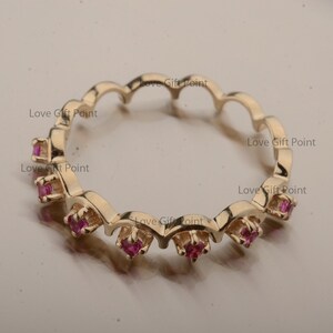 Puede incluir: Un anillo de banda de oro con un borde festoneado y pequeñas piedras preciosas rosas engastadas en la banda.