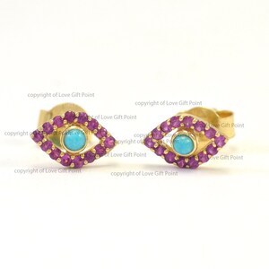 May include: A pair of gold earrings with a turquoise stone in the center of each earring. The earrings are surrounded by small pink stones.
