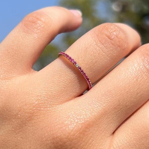 Puede incluir: Un fino anillo de oro con una fila de pequeñas piedras preciosas rojas.