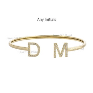 Puede incluir: Un brazalete de oro con dos dijes de iniciales, "D" y "M", engastados con pequeños diamantes.