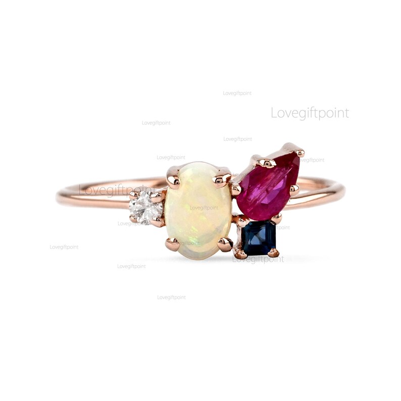 Op de afbeelding: Een ring van ros&eacute;goud met een witte opaal, een robijn, een saffier en een diamant. De ring is gezet op een dunne band.