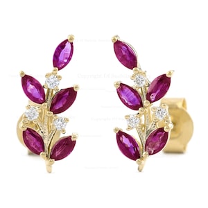 May include: A pair of gold earrings with ruby and diamond accents. The earrings are shaped like a branch with leaves and flowers.