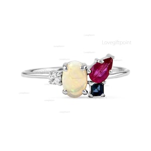 Op de afbeelding: Een zilveren ring met een witte opaal, een rode robijn en een blauwe saffier. De stenen zijn in een clusterdesign gezet.