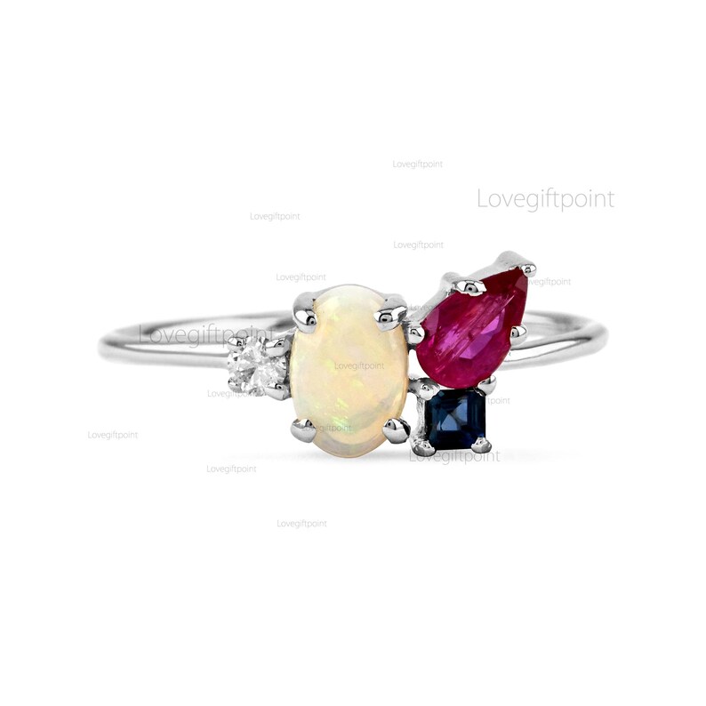 Op de afbeelding: Een zilveren ring met een witte opaal, een rode robijn en een blauwe saffier. De stenen zijn in een clusterdesign gezet.