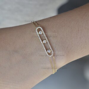 May include: A gold bracelet with a rectangular charm featuring three round diamonds. The charm is suspended from a delicate chain.