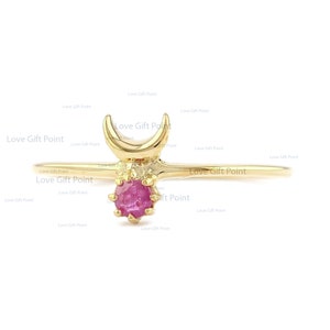May include: A gold ring with a crescent moon design and a pink gemstone. The ring is delicate and feminine.
