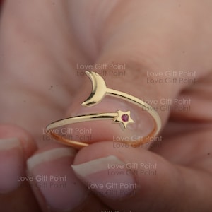 May include: Gold ring with a crescent moon and a star with a red stone. The ring is designed to be worn on the middle finger.
