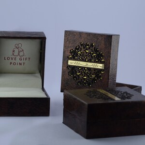 May include: Three brown boxes with intricate designs. The top box is open and has a white interior with the words "LOVE GIFT POINT" printed in red. The other two boxes are closed and have a gold design.