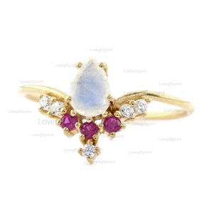 Puede incluir: Un anillo de oro con una piedra de luna en forma de pera y acentos de rubí. El anillo tiene un diseño delicado en forma de vid con pequeños diamantes.