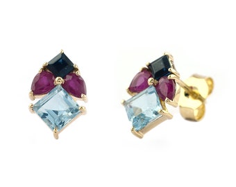 May include: A pair of gold stud earrings featuring a cluster of gemstones. Each earring has a square light blue gemstone at the base, with two pear-shaped red gemstones and a square dark blue gemstone above.