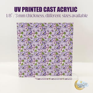 May include: A UV printed cast acrylic piece with a floral design of purple flowers and green leaves. The text on the acrylic reads "UV PRINTED CAST ACRYLIC" and "1/8" / 3 mm thickness, different sizes available". The acrylic is displayed in a clear stand.
