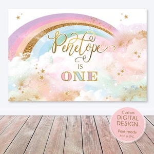 May include: A pink, blue and purple rainbow with gold glitter on a white background. The text "Penelope is ONE" is written in gold with pink and blue accents. There are gold stars scattered throughout the image.