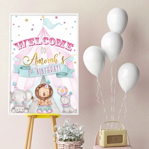 May include: A pink and blue circus-themed welcome sign with a tent, stars, and polka dots. The sign says "Welcome to Amorah's 1st Birthday!" and features illustrations of an elephant, lion, and seal.