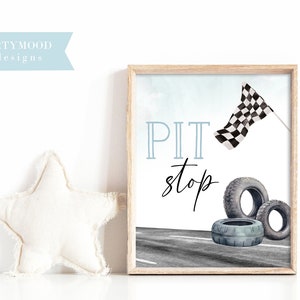 May include: A framed print with a blue and white watercolor background. The print features the text "PIT stop" in black script with a checkered flag and tires on a gray racetrack.