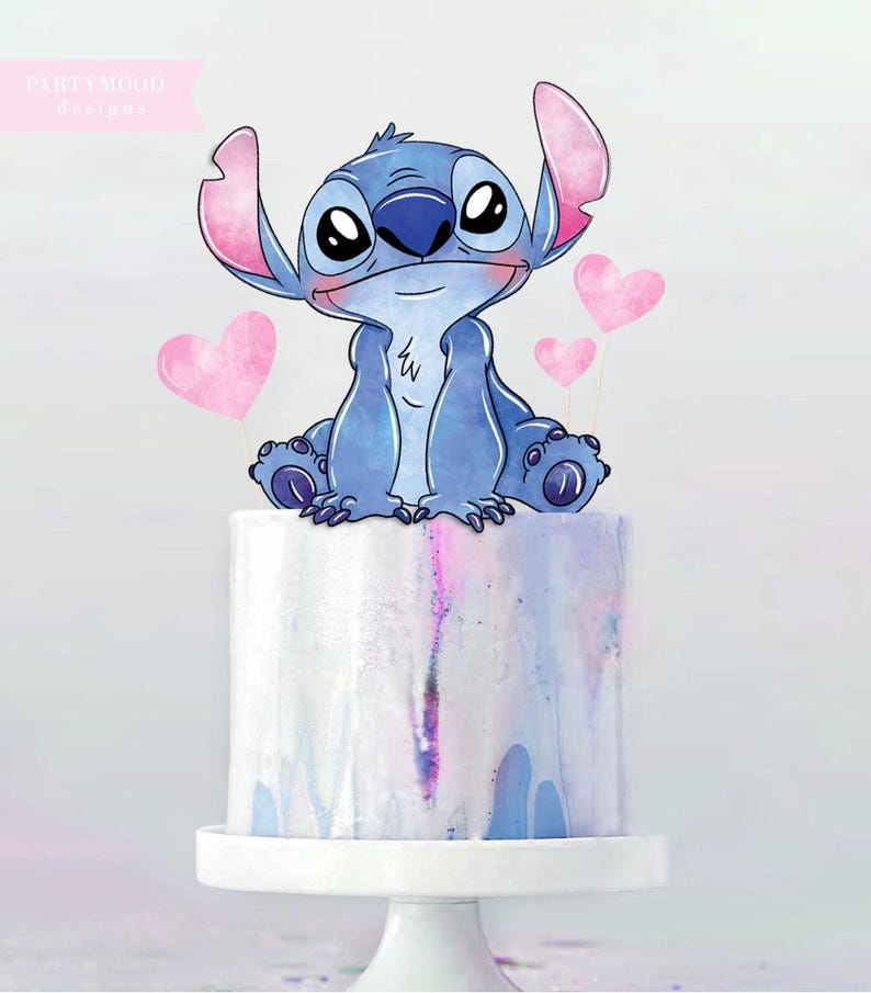 May include: A cake decorated with a blue cartoon character and pink heart-shaped toppers. The cake has a white base and a watercolor design in shades of blue, pink, and purple. The cake sits on a white pedestal.