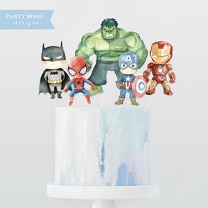 Puede incluir: Una tarta blanca con diseño de acuarela azul y morado, coronada con figuras de superhéroes como Batman, Spider-Man, Hulk, Capitán América e Iron Man. La tarta está sobre un soporte blanco. El texto "PARTYMOOD designs" está en la esquina superior izquierda.