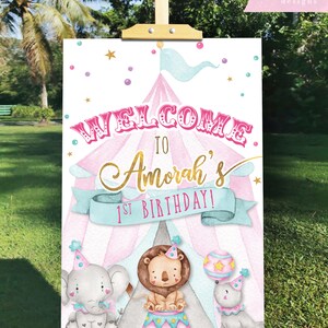 May include: A pink and blue circus tent welcome sign with gold lettering that says "Welcome to Amorah's 1st Birthday!"  The sign features a lion, elephant, and seal with party hats.