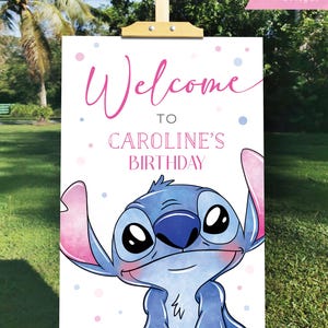 May include: A wooden easel displays a white sign with the words "Welcome to Caroline's Birthday" in pink script. A cartoon character with blue fur and large eyes is featured at the bottom. Pink and blue polka dots are scattered around the text.