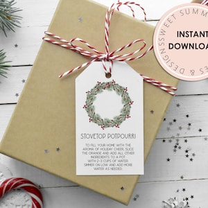 Könnte beinhalten: Ein weißer, druckbarer Geschenkanhänger mit einer Illustration eines grünen und roten Weihnachtskranzes. Der Anhänger enthält den Text "Stovetop Potpourri" und Anweisungen zur Herstellung eines Topf-Potpourris mit Orangenscheiben und anderen Zutaten.