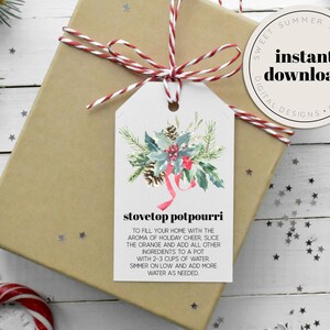 Puede incluir: Una etiqueta de regalo imprimible con una ilustración de acuarela de una corona navideña con bayas rojas y una cinta roja. El texto en la etiqueta dice "stovetop potpourri" e incluye instrucciones para hacer un popurrí para estufa usando rodajas de naranja y otros ingredientes.